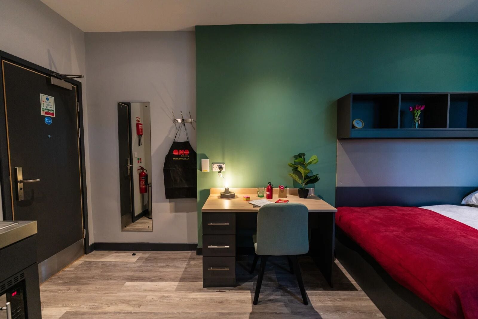 A compact bedroom with a desk, chair, and a bed with a red blanket.