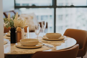 A dining table set with plates, bowls, a wine glass, and a vase with flowers. - Queen's Wharf Residences - Nooon Stay (Brisbane)