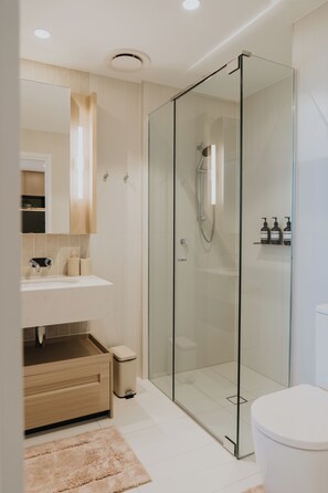 A modern bathroom with a glass-enclosed shower, a white sink, and a beige rug. - Queen's Wharf Residences - Nooon Stay (Brisbane)