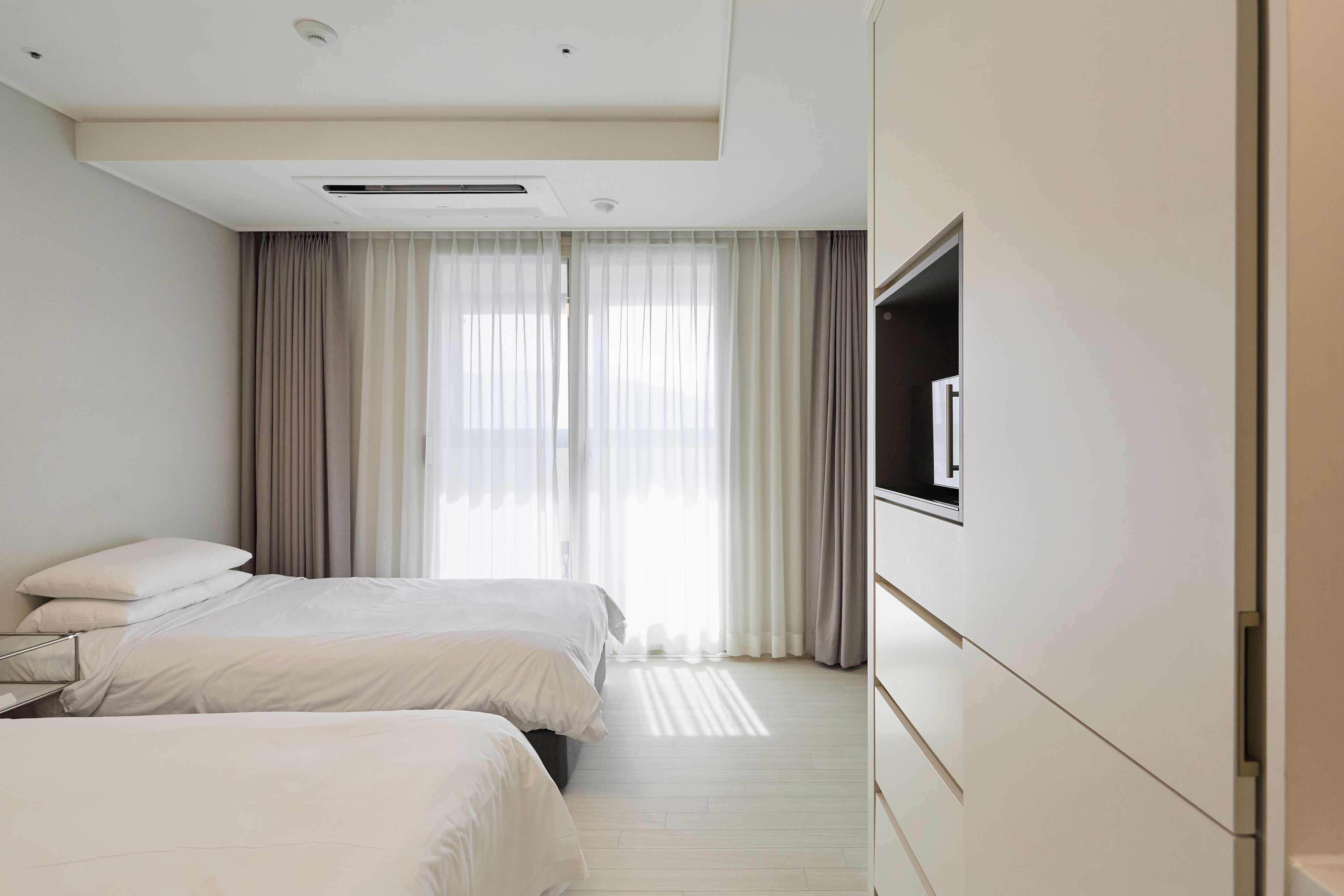A hotel room with two beds, a TV, and a large window with curtains.