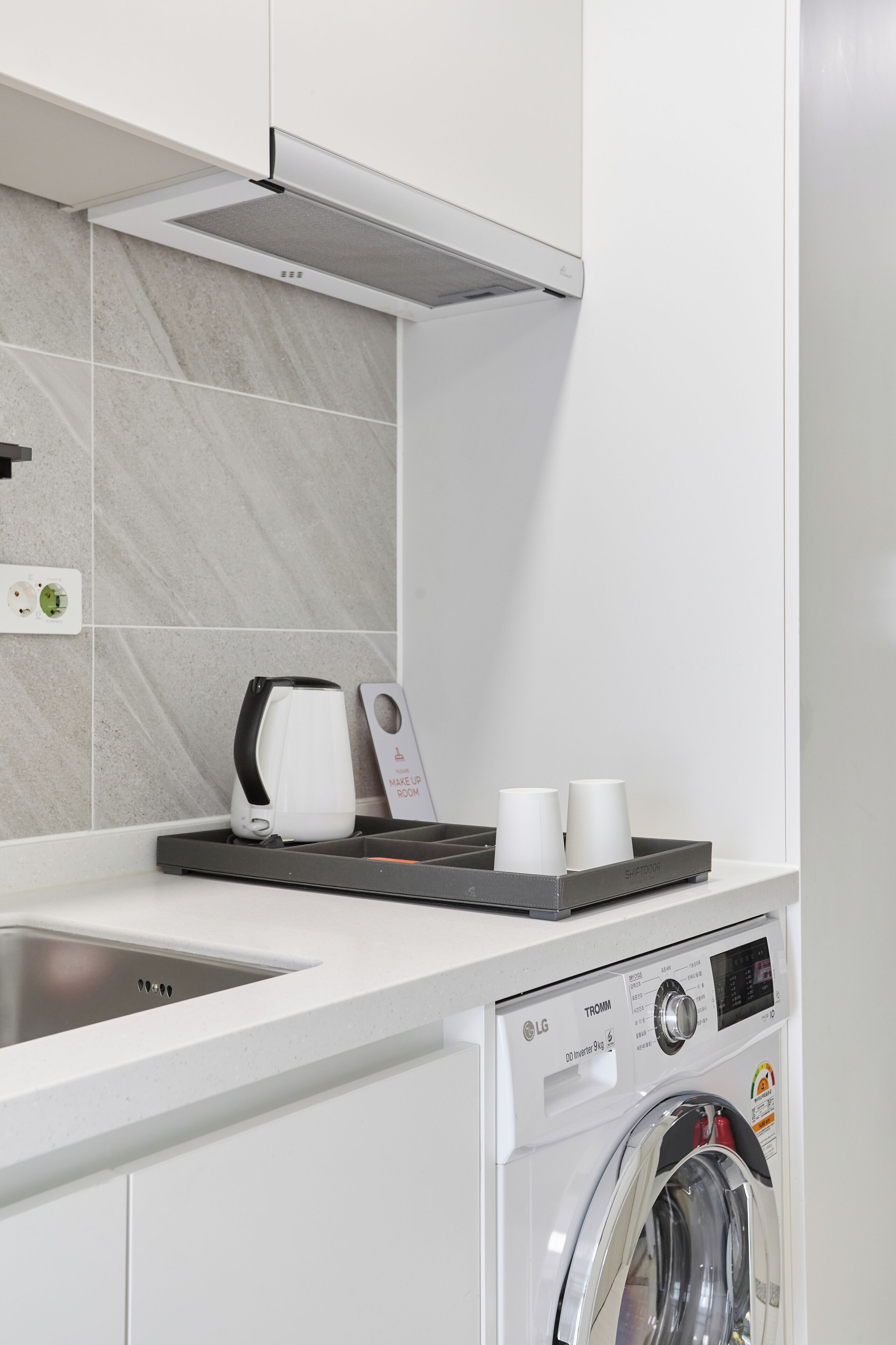 A modern kitchen with a built-in washing machine, a coffee maker, and a tray with cups.
