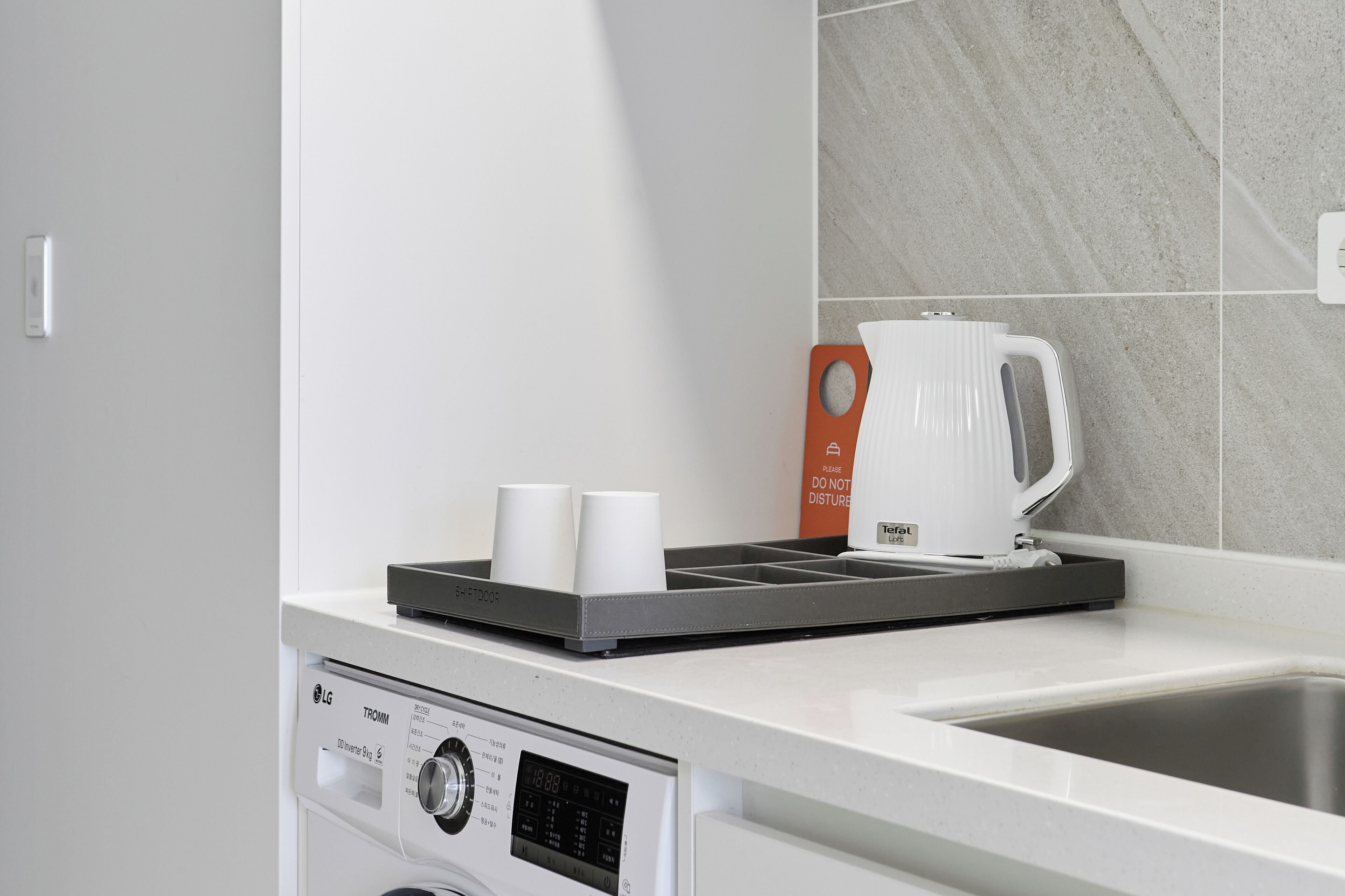 A kitchen with a built-in coffee maker, a kettle, and a tray with two cups.