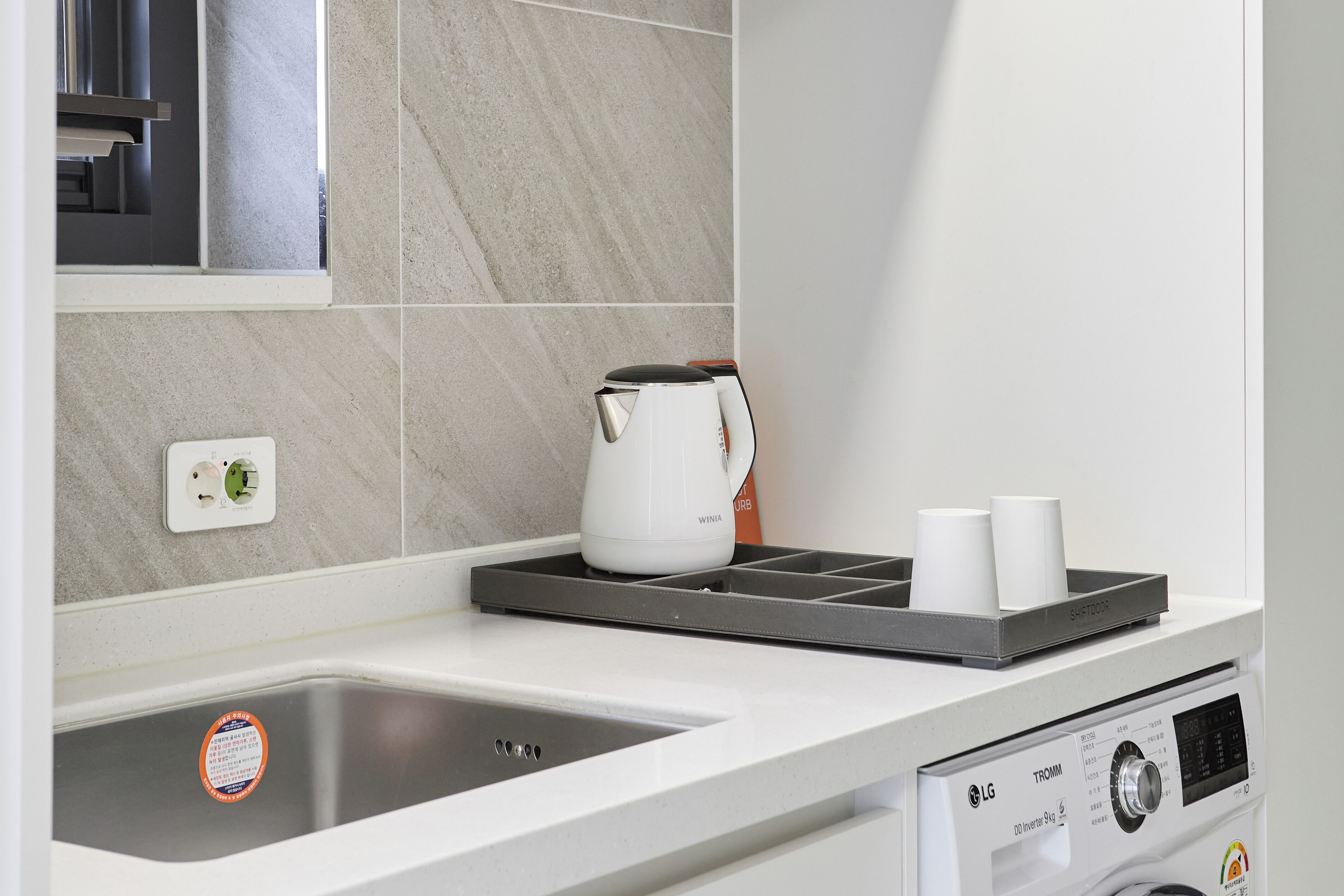 A modern kitchen with a built-in dishwasher, a kettle, and a tray with cups.