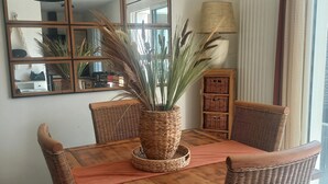 A dining area with a wooden table and wicker chairs, a woven plant pot, and a mirror on the wall. - Lovely 3-bedroom family home for rent Ideal location (La Rochelle)