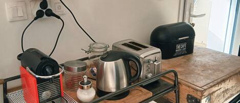A kitchen area with a coffee maker, toaster, kettle, and various mugs on a wooden cart.