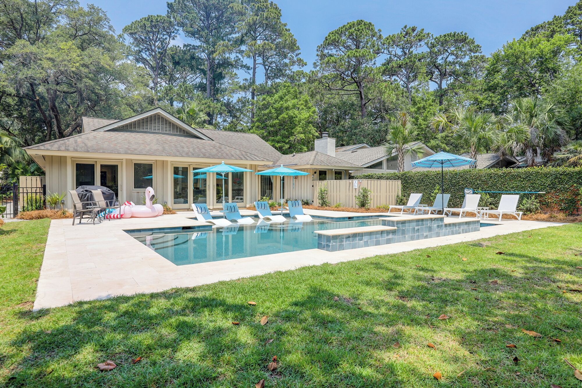 A backyard with a swimming pool, lounge chairs, and umbrellas.