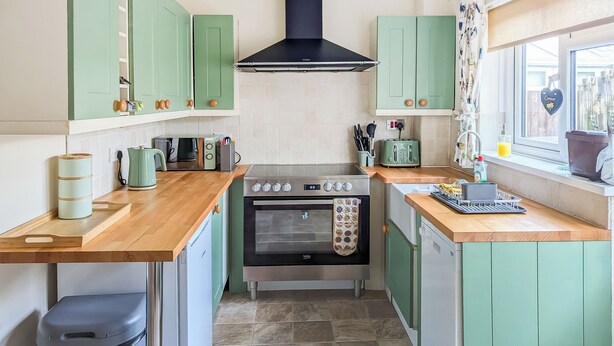 Una cocina compacta con armarios verdes, un horno empotrado, un tostador y una ventana con vistas.