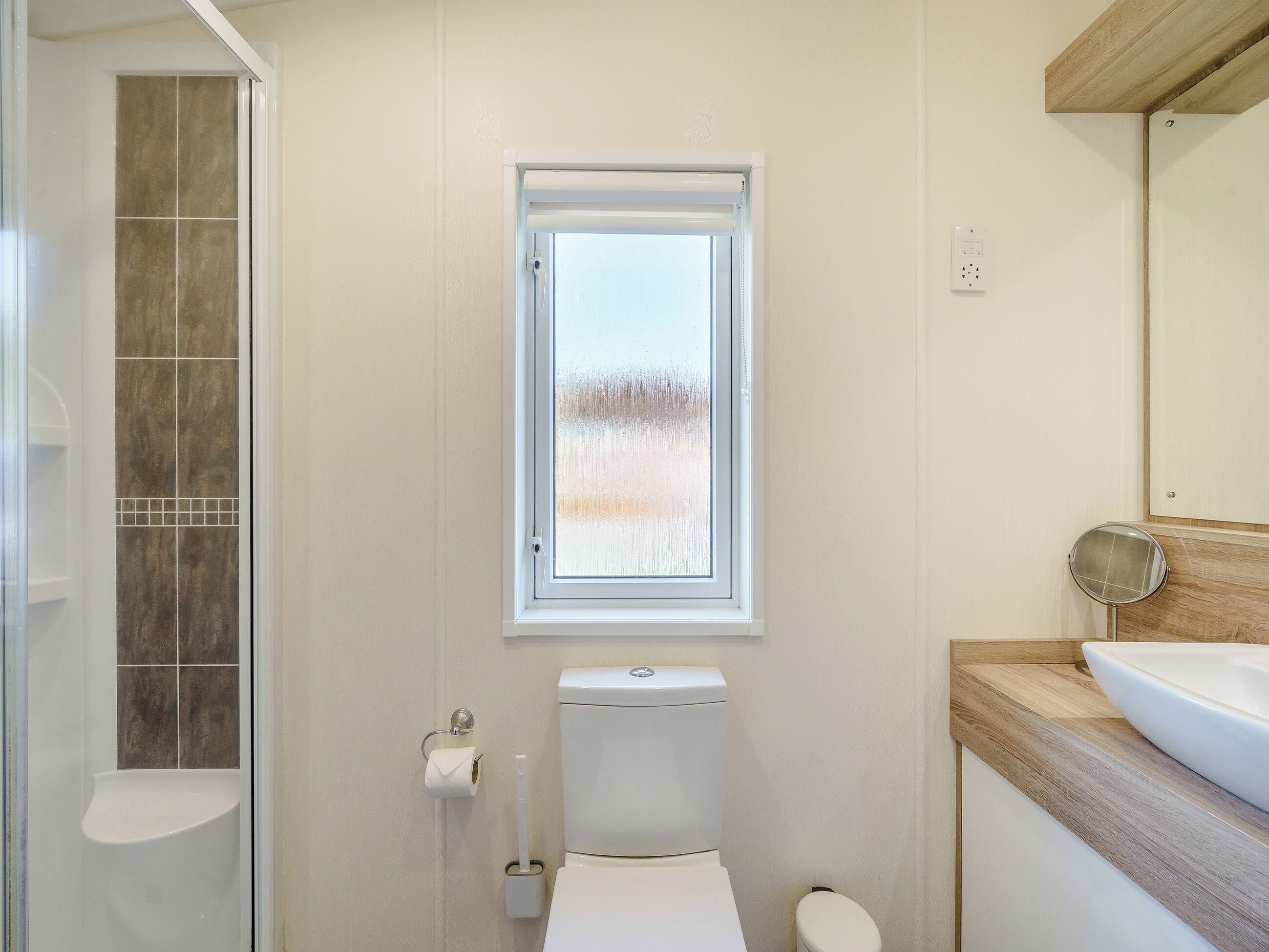 A bathroom with a toilet, a sink, a shower, and a window.