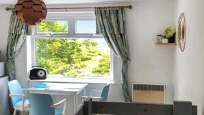 Una habitación con escritorio, dos sillas, una radio, una ventana con cortinas y una cama con cabecera.