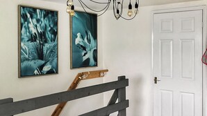 Una escalera con barandilla de madera que conduce a una puerta blanca. Dos cuadros enmarcados con motivos florales decoran la pared sobre la escalera.