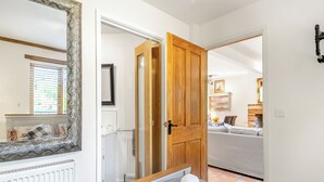 A bedroom with a large mirror, a wooden door, a bed with two rolled towels, a radiator, and a view into another room with a sofa and a fireplace. - 7 bedroom accommodation in Ilketshall St Margaret near Bungay (Ilketshall St Margaret near Bungay)