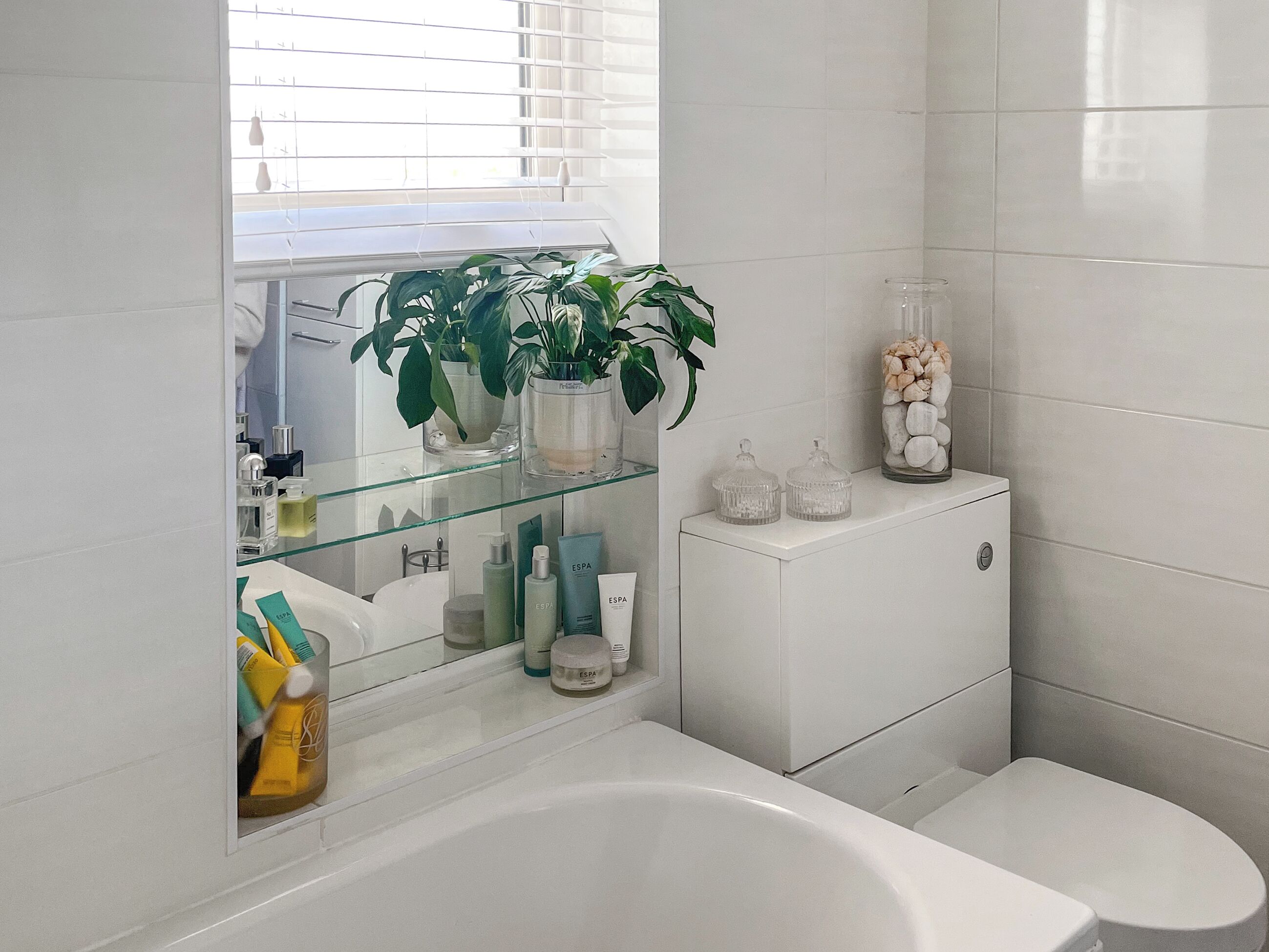 Ein modernes Badezimmer mit einer Glasablage für Toilettenartikel, einer weißen Toilette und einer Badewanne.