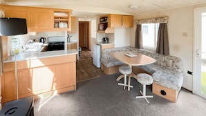 A compact RV kitchen with wooden cabinets, a sink, and a dining area with a table and two stools.