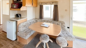 A compact kitchenette with a microwave, coffee maker, and storage cabinets. A dining area with a table and two stools is adjacent to a sofa.