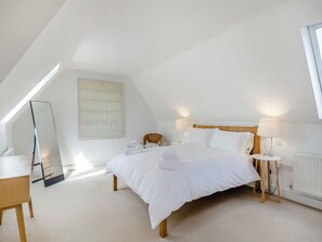 A modern, well-lit bedroom with a sloped ceiling, a large bed with white linens, a wooden headboard, two bedside tables with lamps, and a large mirror on one wall.