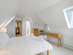 A bedroom with a bed, a wooden dresser, a chair, and a desk. There is a skylight and a door leading to another room.