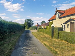 A narrow rural road flanked by houses with red-tiled roofs and stone walls.