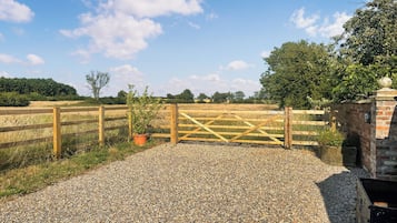 Une allée de gravier mène à un portail en bois, avec un pot de fleurs placé à côté.