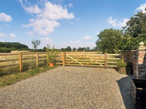 A gravel driveway leading to a wooden gate with a potted plant beside it.