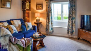 A cozy living room with a blue sofa, a wooden coffee table, a lamp, a clock, and a television. - 2 bedroom accommodation in Winestead (Winestead)