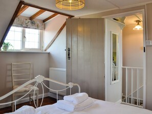 A bedroom with a sloped ceiling, a bed with white linens, a chair, a radiator, and a window with a plant.