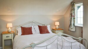 A neatly made bed with white bedding and two brown pillows, flanked by two bedside tables with lamps, in a room with a window and floral curtains. - 2 bedroom accommodation in Winestead (Winestead)