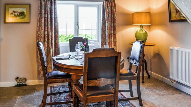 A dining area with a round table, four chairs, a rug, a lamp, and a window with curtains. - 2 bedroom accommodation in Winestead (Winestead)
