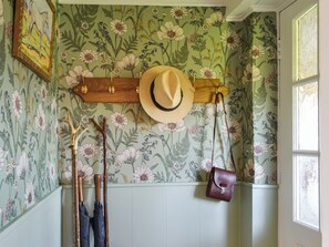 A room with floral wallpaper, a wooden hat rack, a hat, a cane, and a handbag.