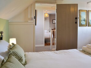 A bedroom with a large bed, a bedside table, a lamp, and a door leading to another room.