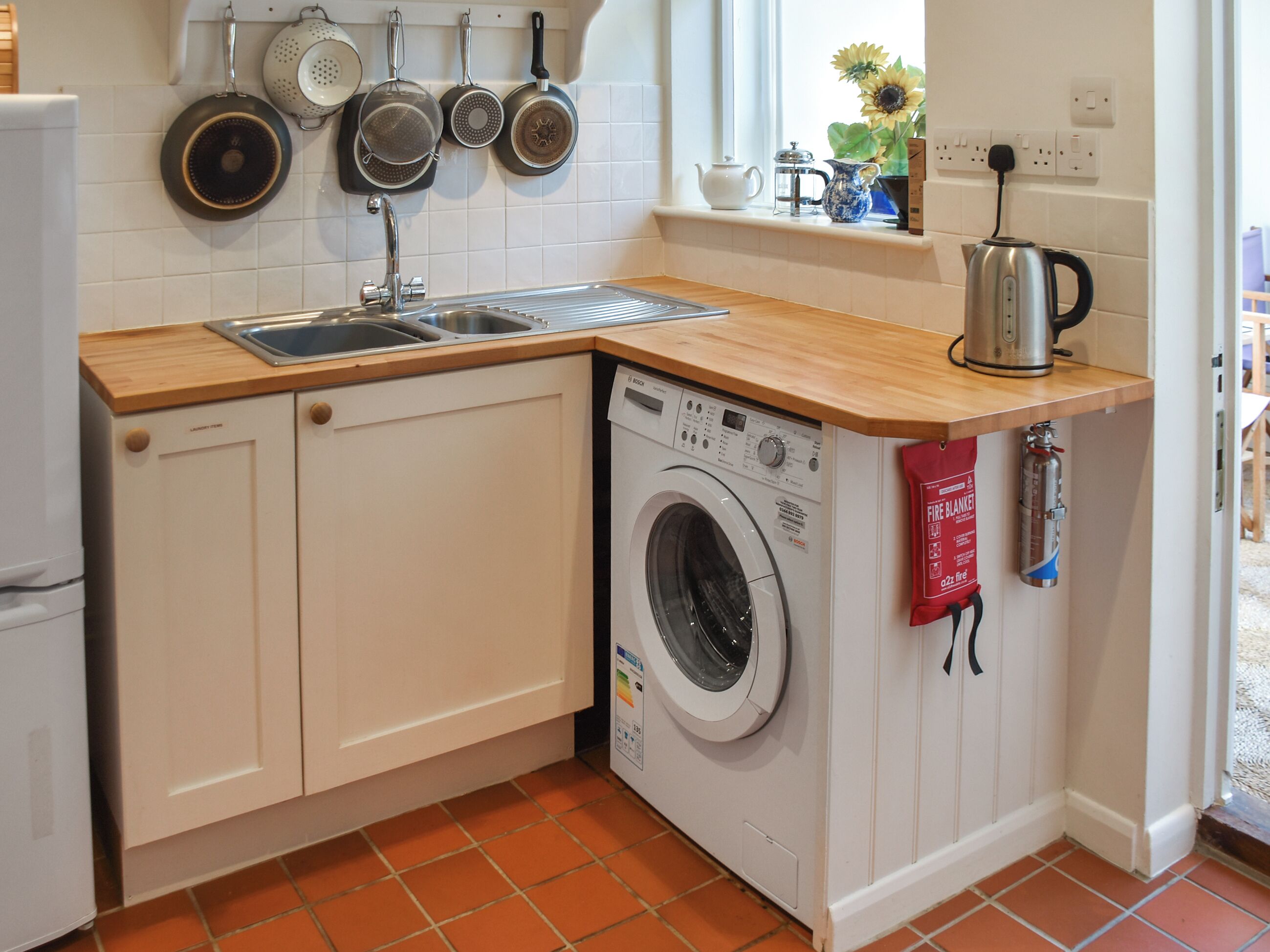 A compact kitchen with a washing machine, a sink, and a variety of cookware hanging above.