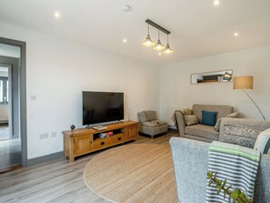 Een moderne woonkamer met een flatscreen televisie, een houten tv-meubel, een rond vloerkleed, een bank en een vloerlamp.
