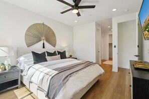 A bedroom with a bed, bedside tables, a ceiling fan, a wall-mounted fan, and a TV. - Suncrest: Spacious 2BR condo in La Quinta with mountain views, steps from PGA courses. (La Quinta)