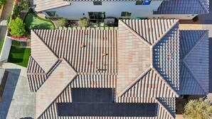 An aerial view of a residential area with a house featuring a tiled roof, a paved patio, and a small garden. - Heated Pool Oasis by the Santa Rosa Mountains (La Quinta)