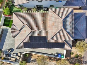 An aerial view of a residential area with a house featuring a tiled roof, a paved patio, and a small garden. - Heated Pool Oasis by the Santa Rosa Mountains (La Quinta)