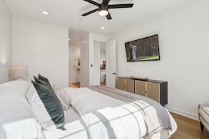 A bedroom with a bed, a ceiling fan, a painting on the wall, and a cabinet.