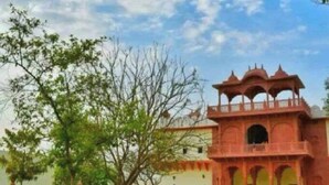 A traditional building with a red facade and arched windows, surrounded by a well-maintained lawn and trees. - Heritage Lotwara Fort (Baswa)