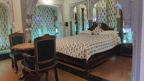 A traditional bedroom with a bed, a round wooden table, and two chairs. - Heritage Lotwara Fort (Baswa)