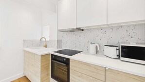 A modern kitchen with white cabinetry, a black oven, a white countertop, a toaster, and a microwave. - Host Stay The Surf Shack (Saltburn-by-the-Sea)