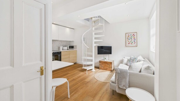 A modern living room with a white sofa, a small round table, and a spiral staircase leading to a kitchen. - Host Stay The Surf Shack (Saltburn-by-the-Sea)