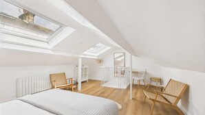 A spacious attic bedroom with a large skylight, a bed, wooden chairs, and a small seating area. - Host Stay The Surf Shack (Saltburn-by-the-Sea)