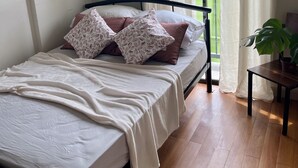 Une chambre à coucher avec un lit, une fenêtre avec des rideaux, une plante en pot et un appareil de climatisation.