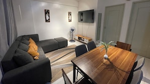 Un salon moderne avec un canapé de couleur foncée, une table à manger en bois et un téléviseur à écran plat fixé au mur.