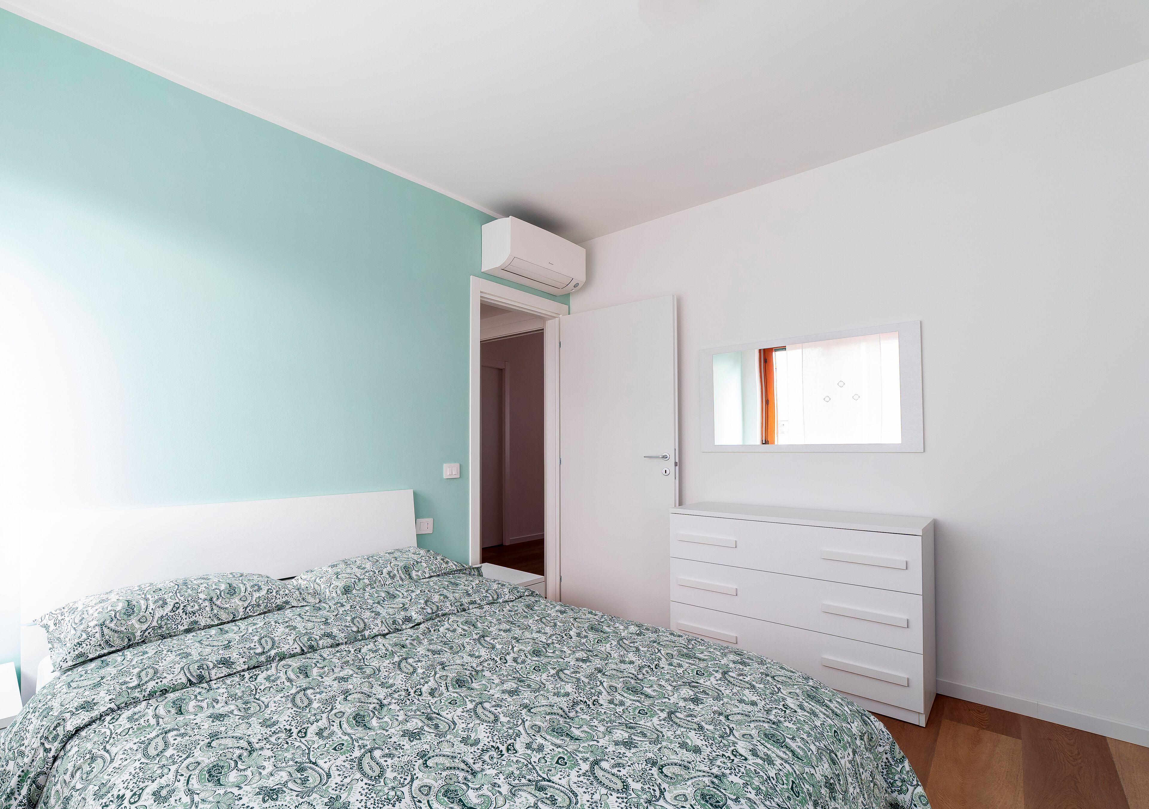 A bedroom with a bed, a dresser, a mirror, and an air conditioning unit.