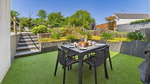 Un patio con una mesa lista para comer, rodeado de césped artificial y diversas plantas.