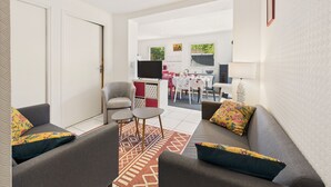 Una sala de estar moderna con sofás grises, un tapete estampado y un comedor con televisor y mesa.