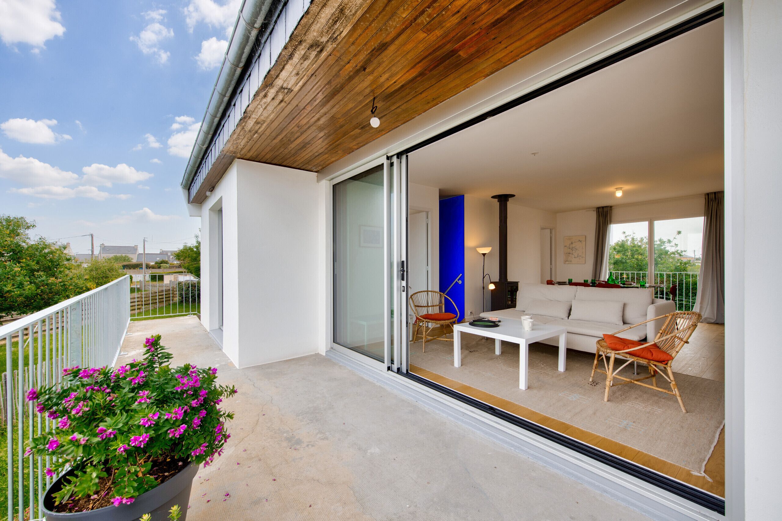 A modern outdoor living space with a white sofa, two chairs, a table, and a potted plant.
