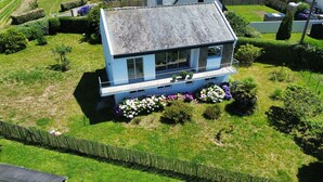 A two-story house with a balcony, surrounded by well-maintained gardens and hedges. - Sea view – House for 6 – 100 m from the beach (Plouguerneau)