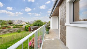 A balcony with a view of a residential area, a green potted plant, and a white railing. - Sea view – House for 6 – 100 m from the beach (Plouguerneau)