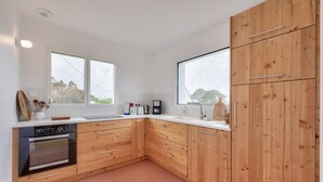 A modern kitchen with wooden cabinets, a built-in oven, and a large window providing natural light. - Sea view – House for 6 – 100 m from the beach (Plouguerneau)