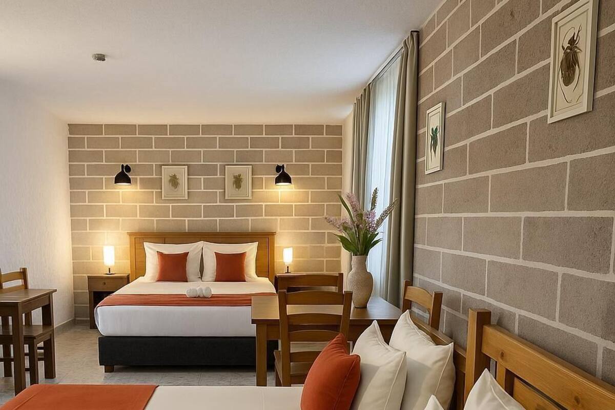 Habitación de hotel con dos camas, cabecero de madera, pared de ladrillo y una mesita con una planta.